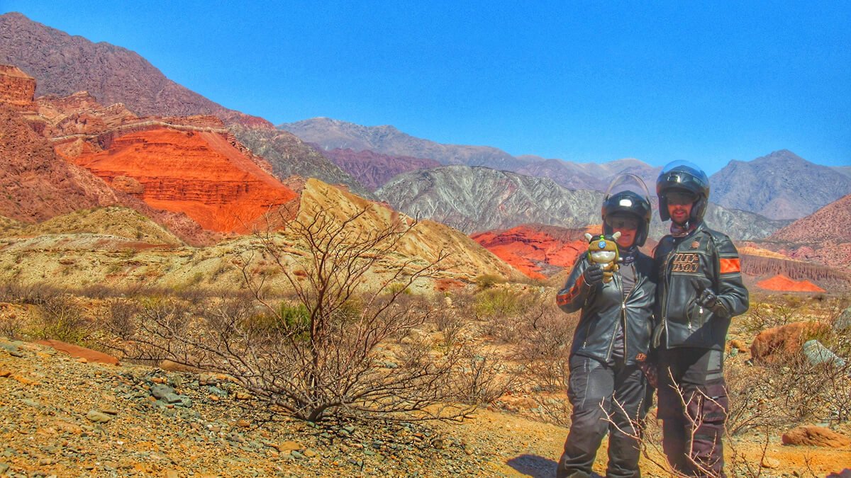 Imagem da Ruta Nacional 68 em Salta, Argentina, mostrando as montanhas coloridas da Quebrada de las Conchas. Céu azul e sol iluminam a cena, destacando formações icônicas na Quebrada de Cafayate.