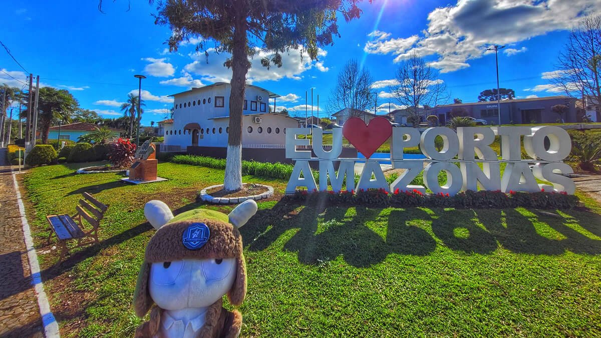 Praça com letreiro “Eu amo Porto Amazonas PR” e prefeitura em formato de barco ao fundo