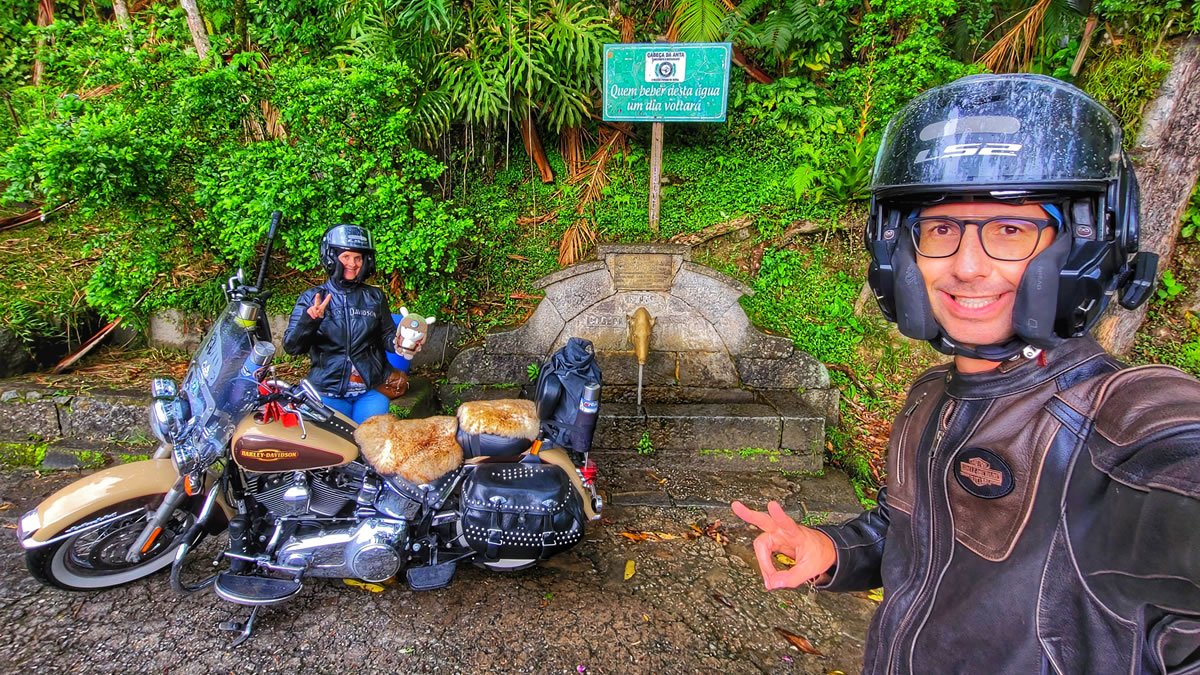 Casal em viagem de moto pela Serra da Cabeça da Anta (SP-079), ao lado da famosa Fonte da Cabeça da Anta, entre Tapiraí e Juquiá, em meio à Mata Atlântica no interior de São Paulo.